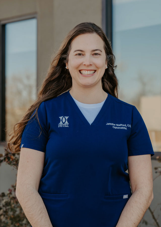 Jennifer E. Stafford, O.D., wearing a blue medical uniform with the Henry Eye Clinic logo, smiling outdoors, representing eye care expertise.